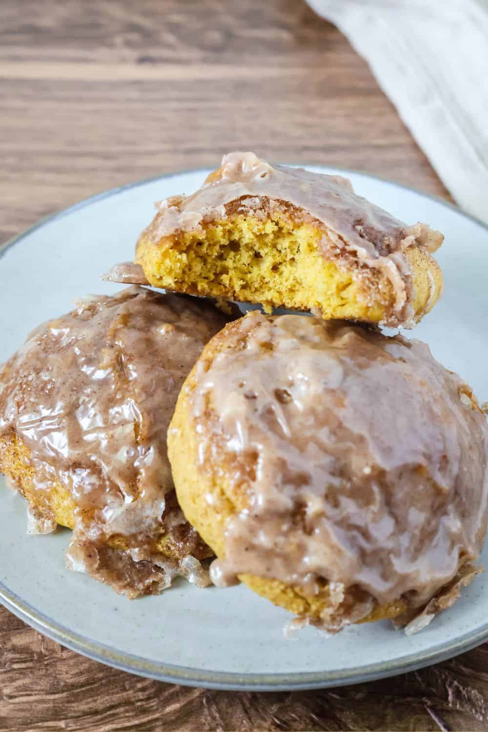 Close-up view of pumpkin fritters with glaze. One fritter has a bite taken out of it to show the moist interior.