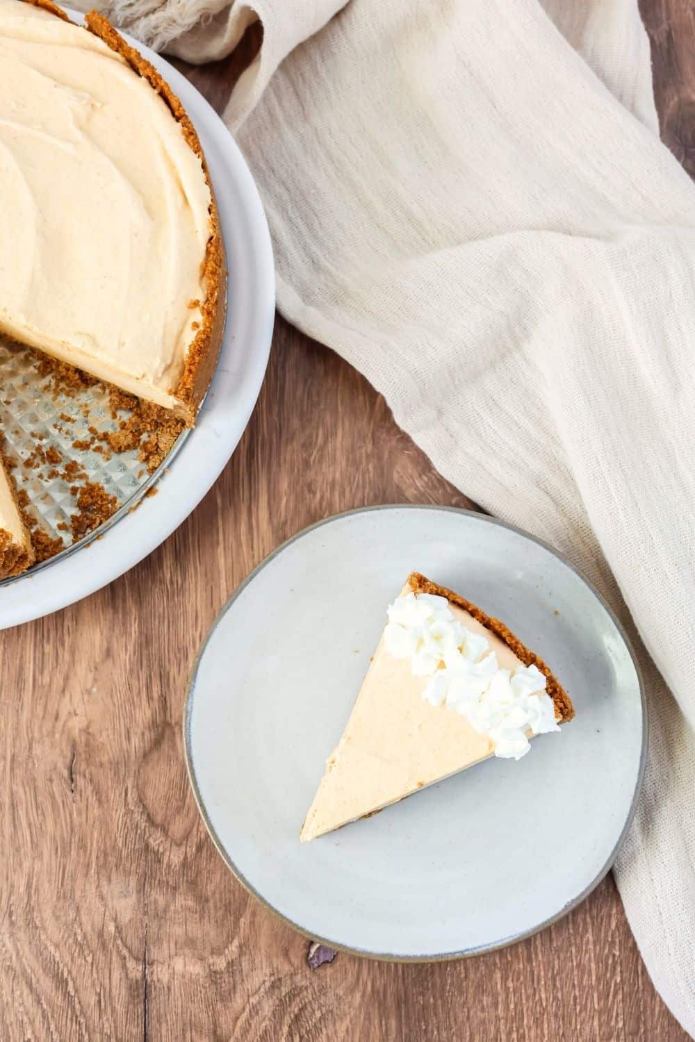 Overhead view of a slice of pumpkin ice cream pie on an ivory plate, with the remainder of the whole pumpkin cheesecake pie next to the plate.