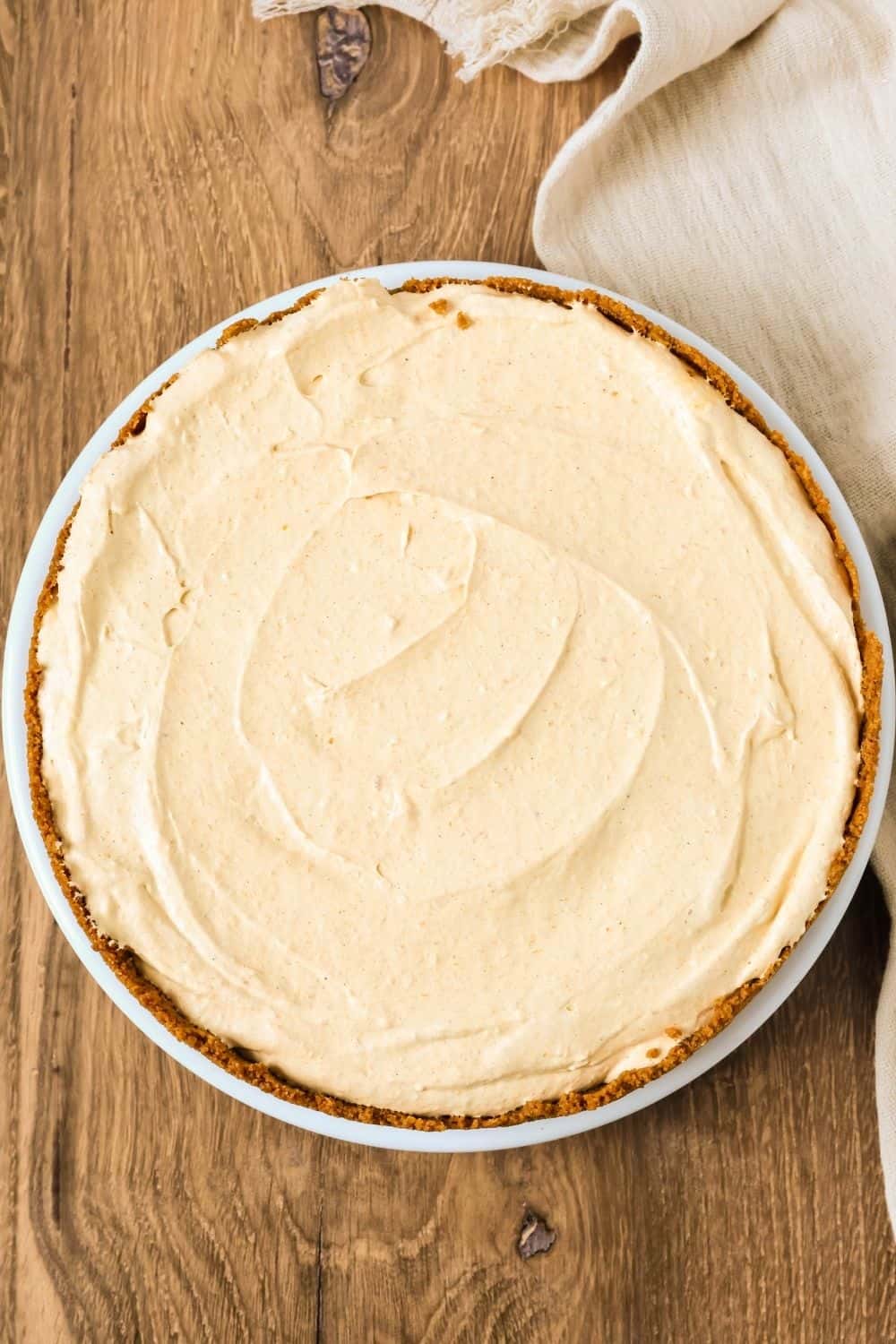 Overhead view of a whole frozen pumpkin pie cheesecake ice cream pie on a white plate.