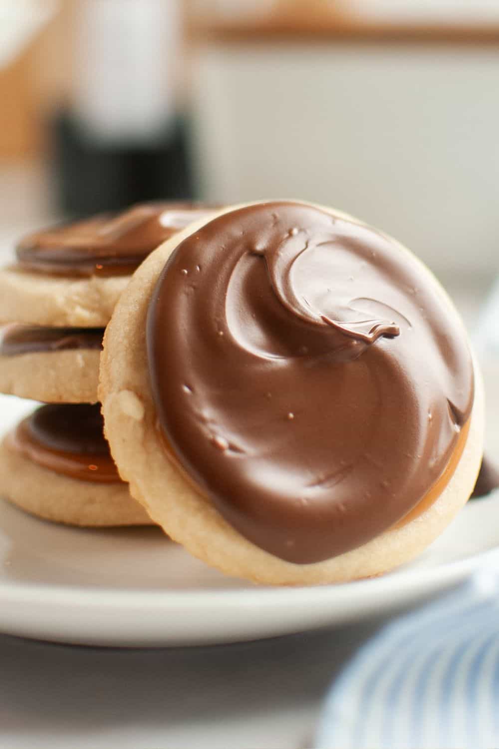 Three Twix shortbread cookies stacked on a white plate, with a fourth cookie propped up against the stack.