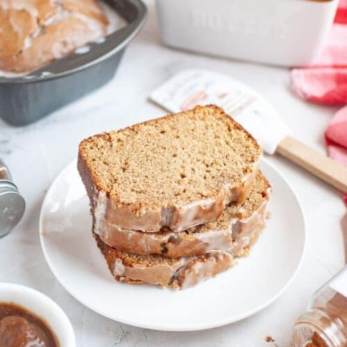 Slices of apple butter bread on a white plate, with the remaining loaf of quick bread in the background.
