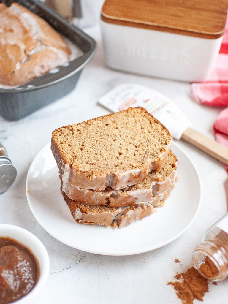 Slices of apple butter bread on a white plate, with the remaining loaf of quick bread in the background.