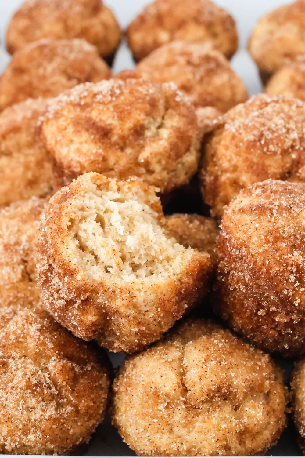 Close-up view of apple cider donut holes that are coated with cinnamon sugar. One of the donut holes has a bite taken out of it, showcasing the soft and fluffy inside.