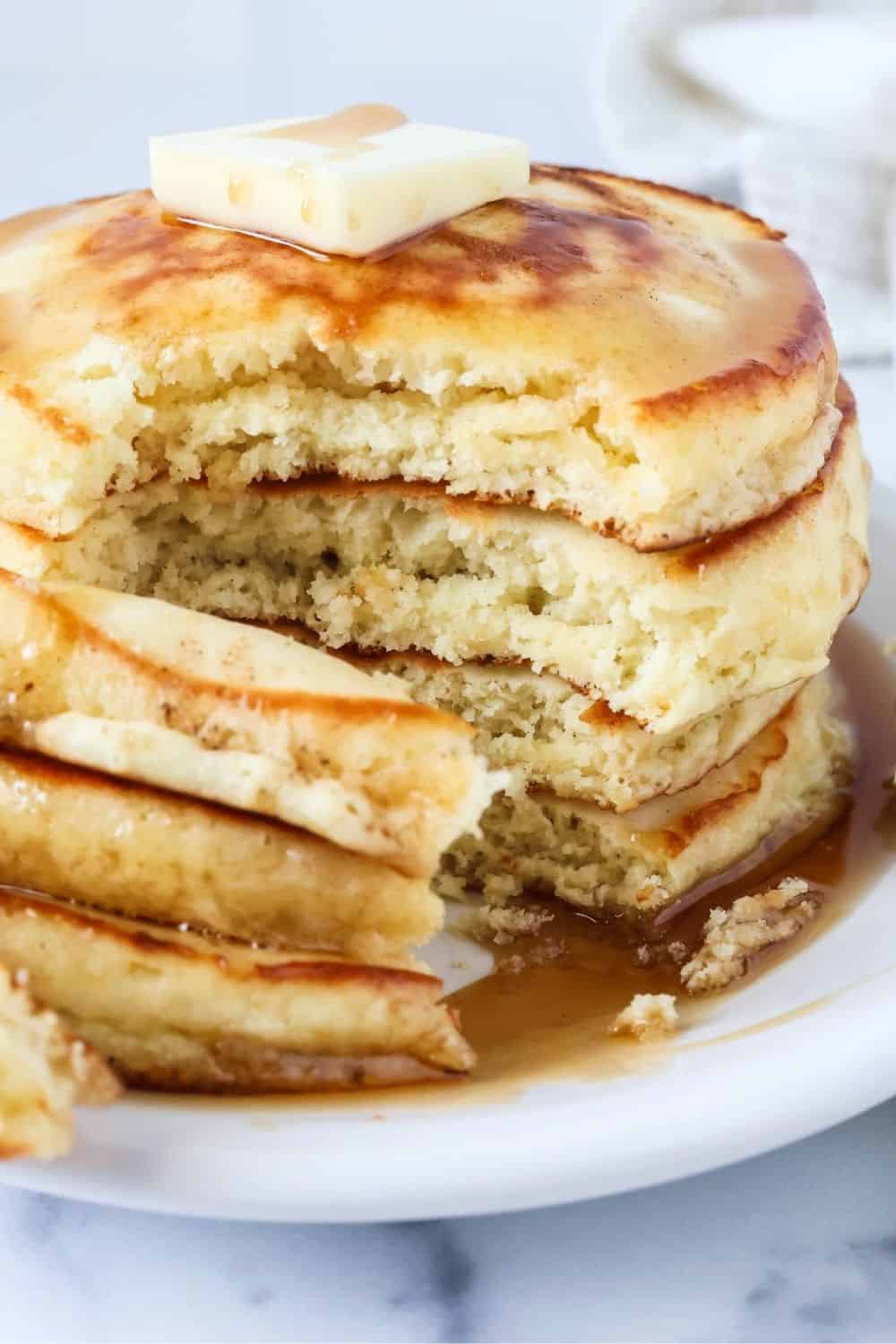 Stack of pancakes made with Bisquick, topped with a pat of butter and syrup. The stack has been cut through to show the fluffy interior texture of the pancakes.