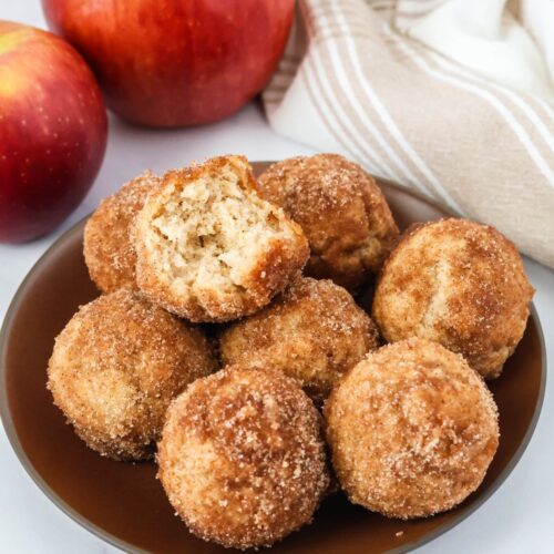 Bisquick apple cider donut holes served on a brown plate. One of the doughnut holes has a bite taken out of it.