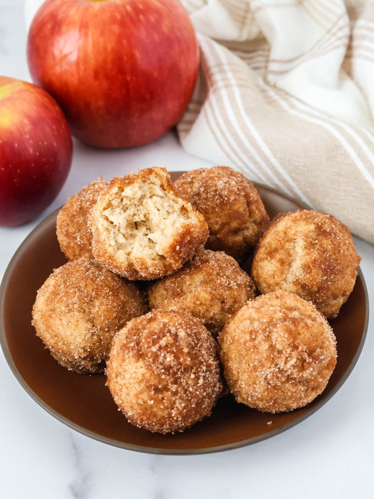 Bisquick apple cider donut holes served on a brown plate. One of the doughnut holes has a bite taken out of it.