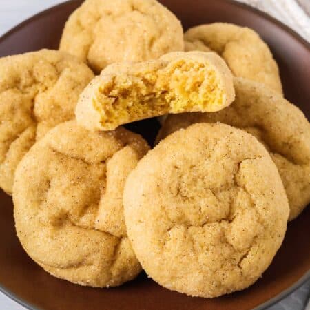 Several cake mix pumpkin sugar cookies on a brown plate; one cookie has a bite taken out of it to show the soft texture.
