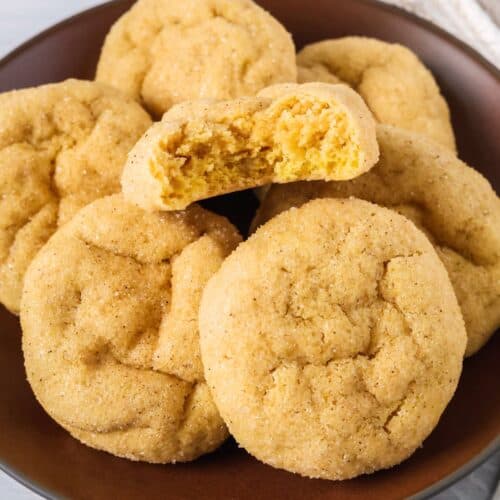Several cake mix pumpkin sugar cookies on a brown plate; one cookie has a bite taken out of it to show the soft texture.