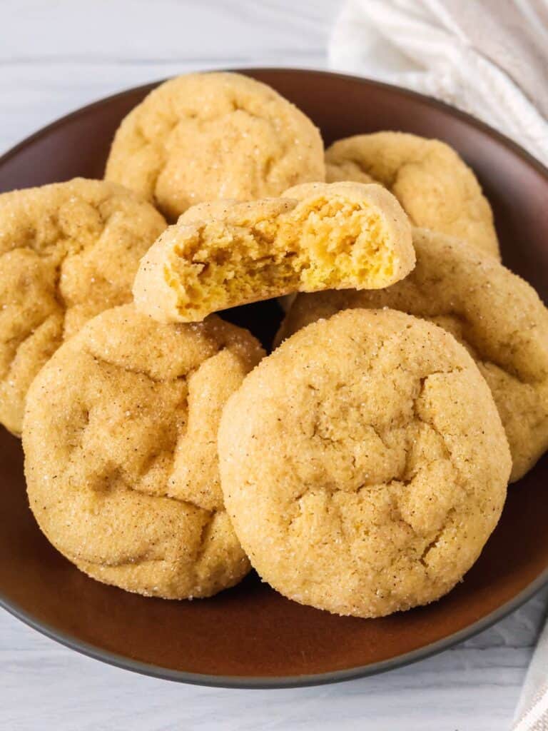 Several cake mix pumpkin sugar cookies on a brown plate; one cookie has a bite taken out of it to show the soft texture.