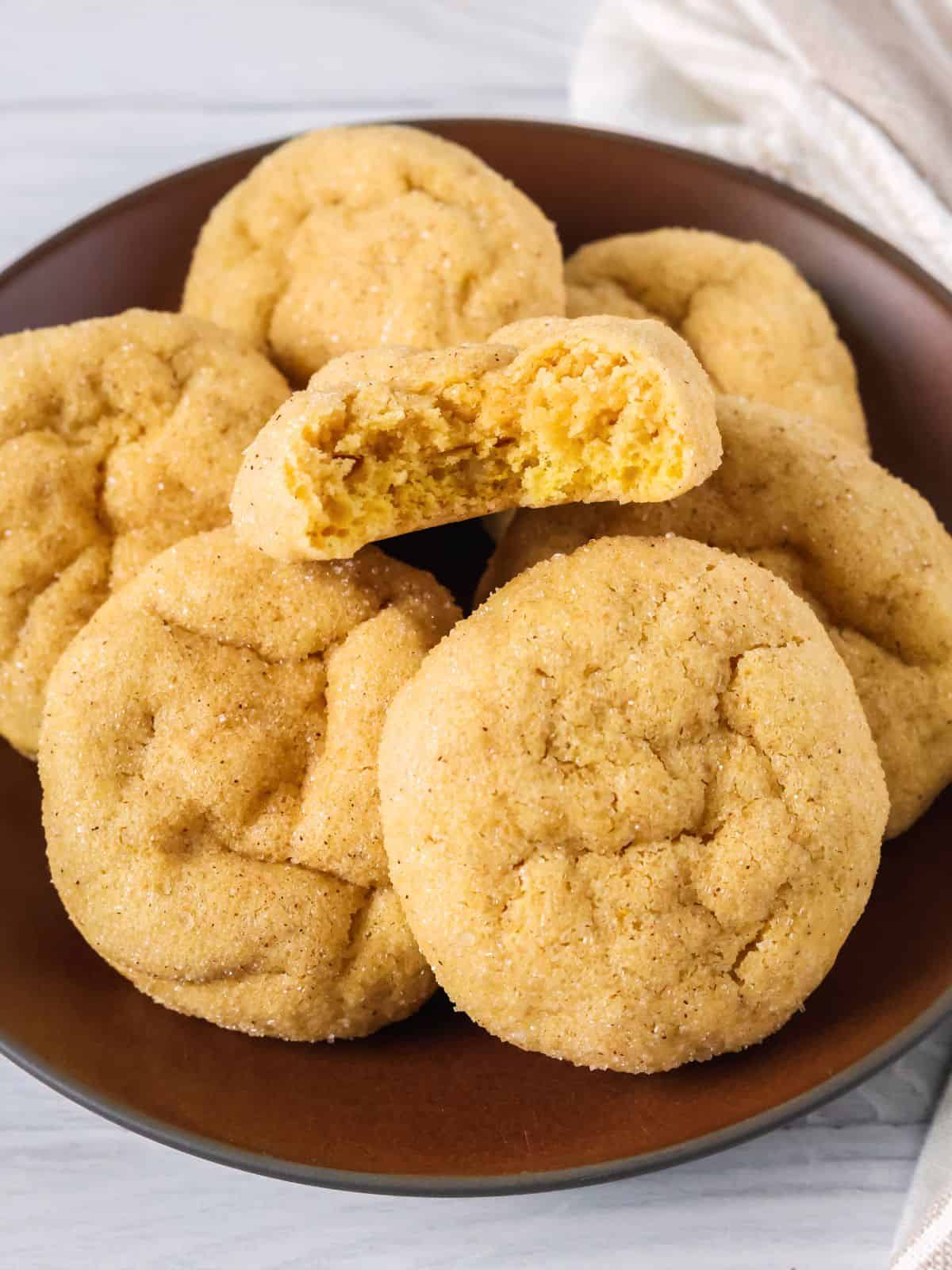 Several cake mix pumpkin sugar cookies on a brown plate; one cookie has a bite taken out of it to show the soft texture.