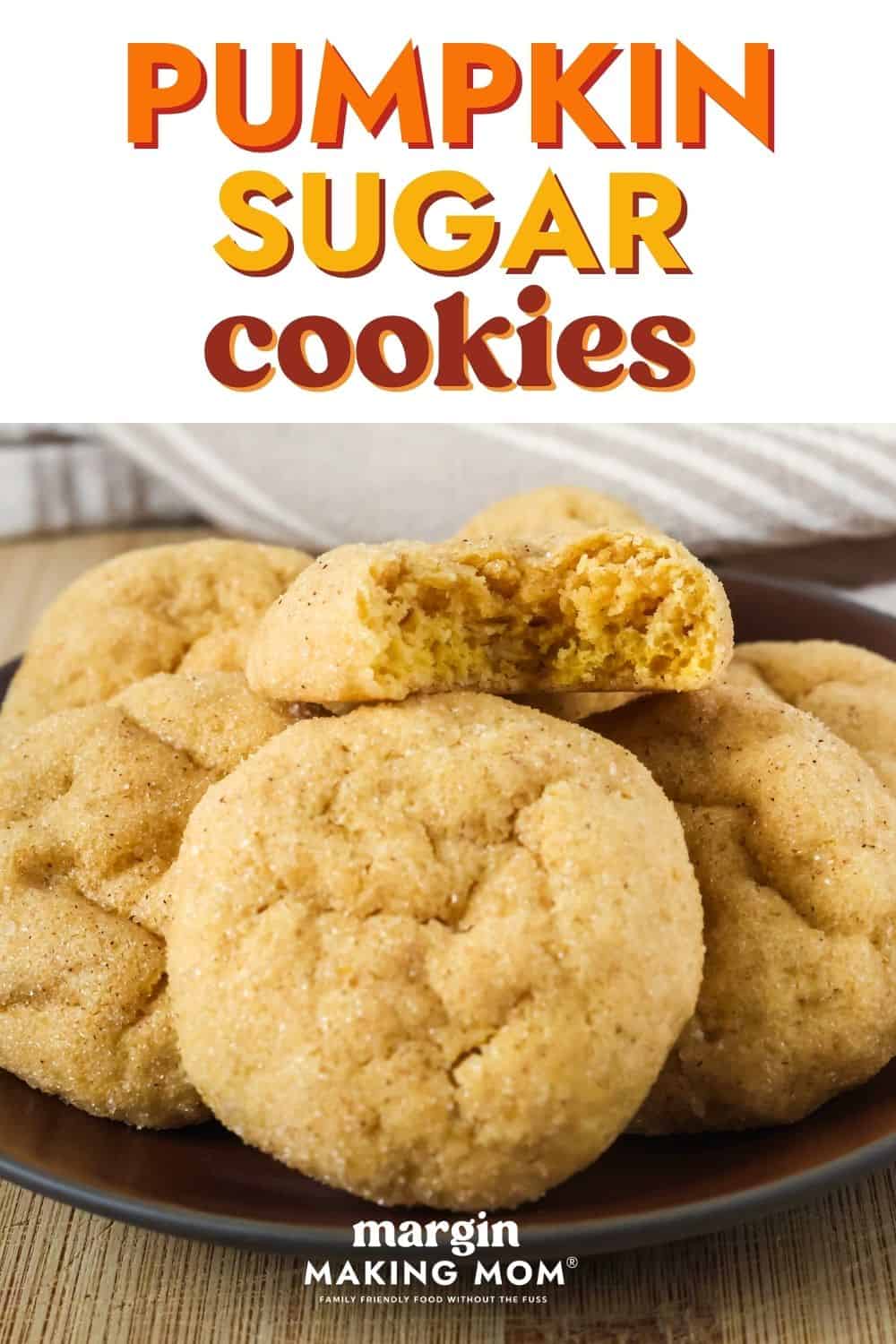 Cake mix pumpkin sugar cookies served on a brown plate; one cookie has a bite taken out of it to show its soft and chewy texture.