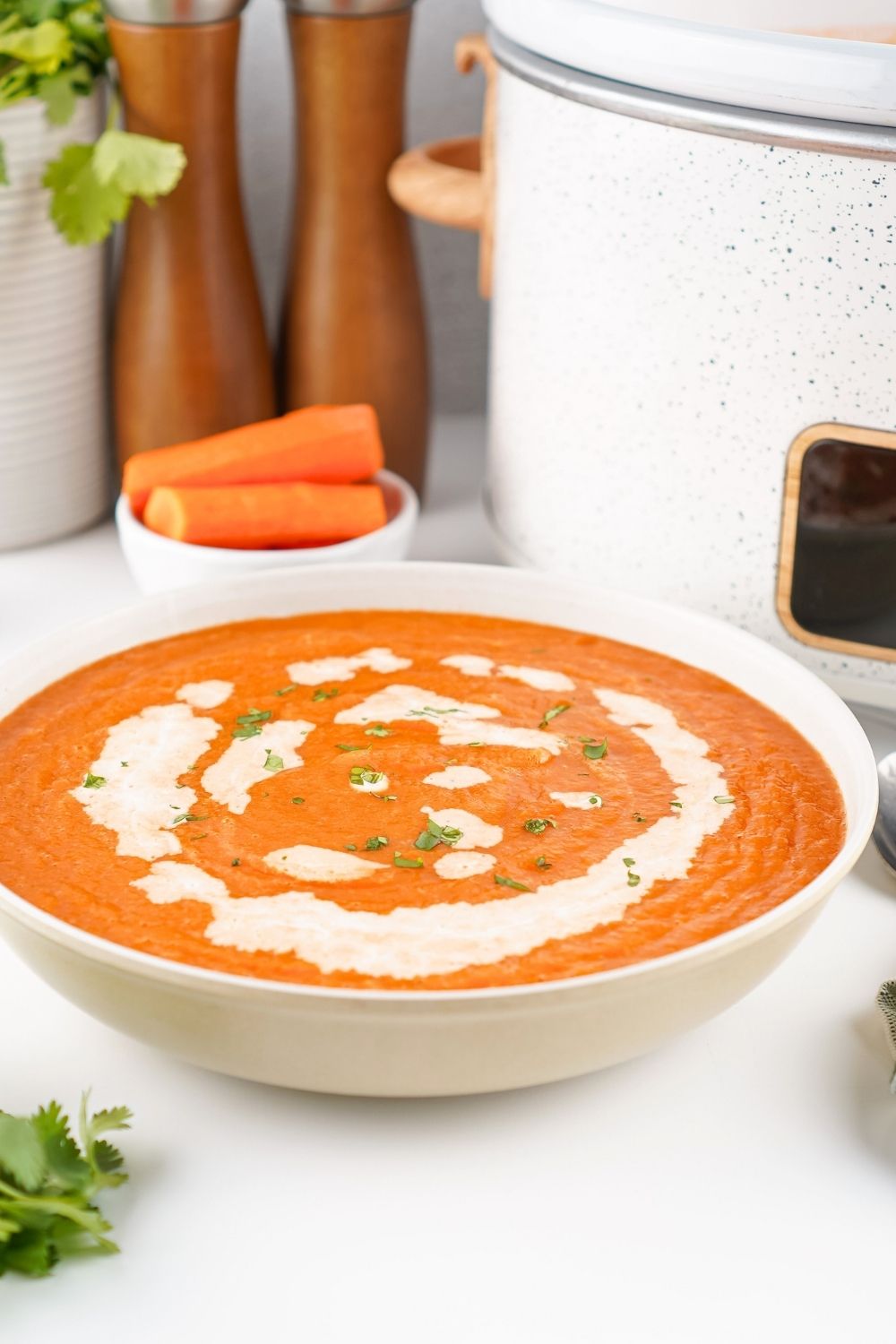 White bowl of vegetarian carrot soup with a slow cooker in the background.