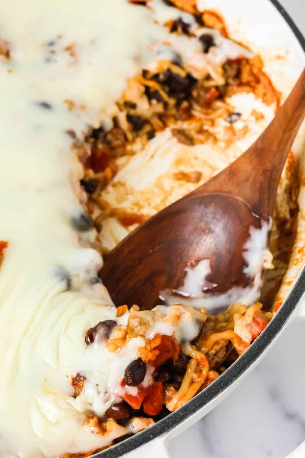 Cheesy Knorr beef taco casserole with a wooden serving spoon scooping out a helping from the pan.