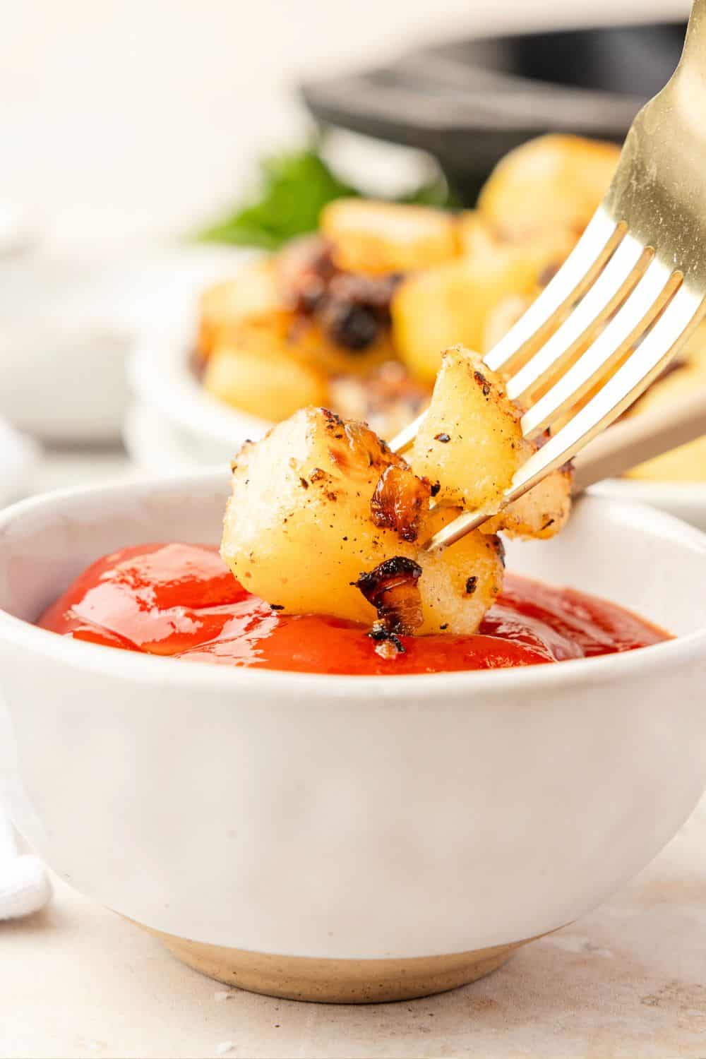 A fork dips country fried potatoes and onions into a small dish of ketchup.