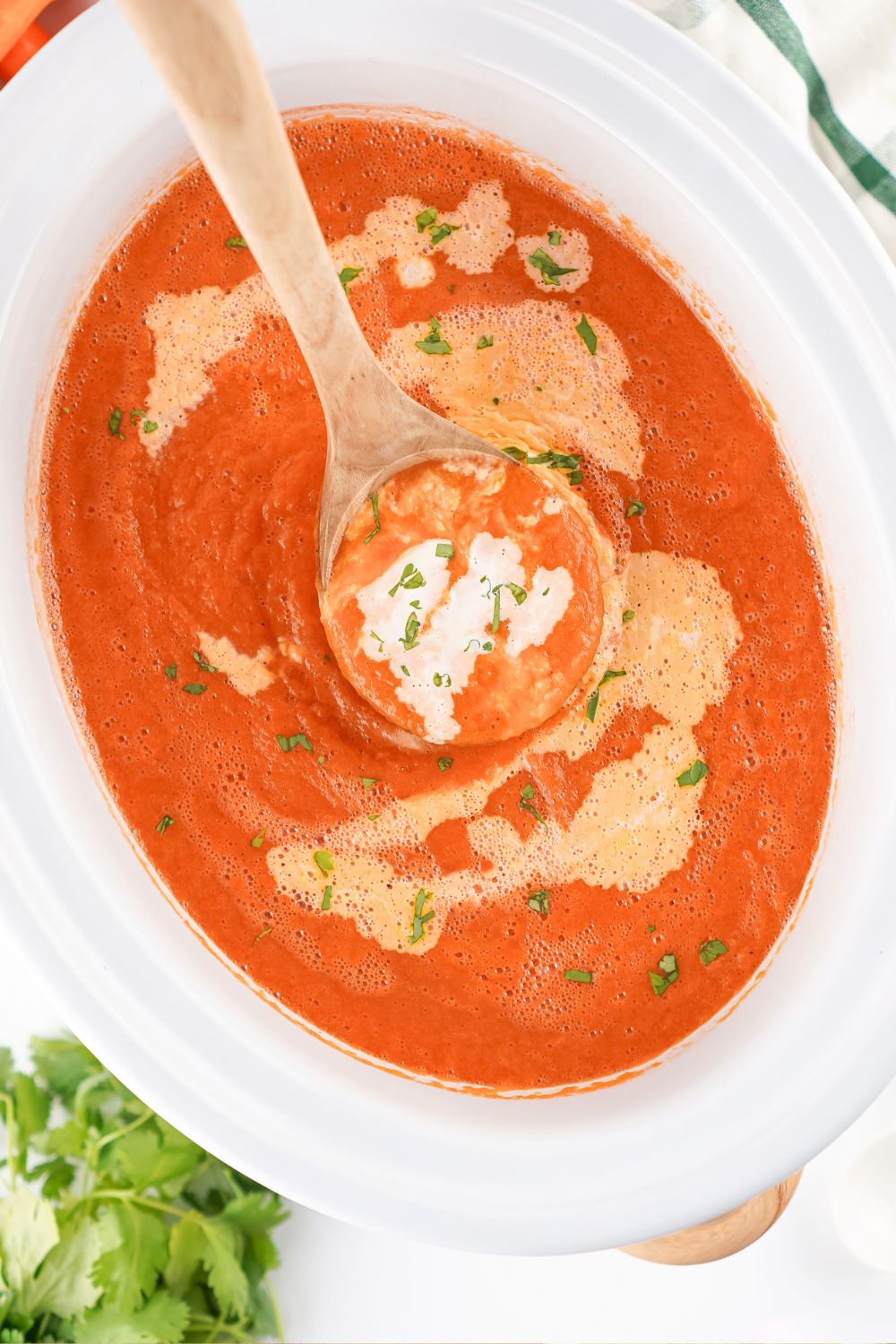 Overhead view of creamy carrot soup in a Crock Pot slow cooker. A wooden ladle is scooping out some soup.