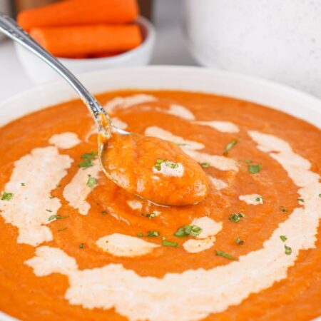 A white bowl filled with Crock Pot carrot soup. A spoon is lifting out a bite of soup from the bowl.