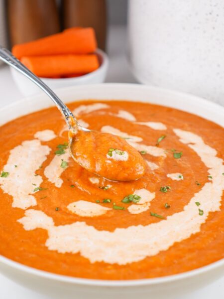 A white bowl filled with Crock Pot carrot soup. A spoon is lifting out a bite of soup from the bowl.