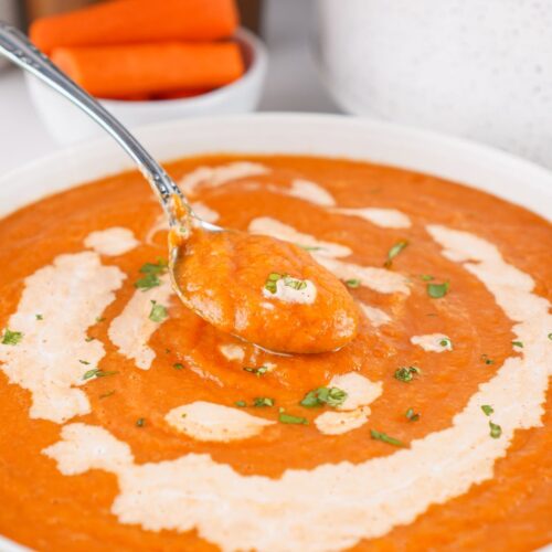 A white bowl filled with Crock Pot carrot soup. A spoon is lifting out a bite of soup from the bowl.