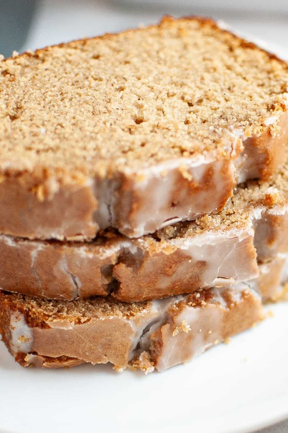 Close-up view of three slices of apple butter bread stacked on a white plate, showcasing the moist interior and the powdered sugar glaze on top.
