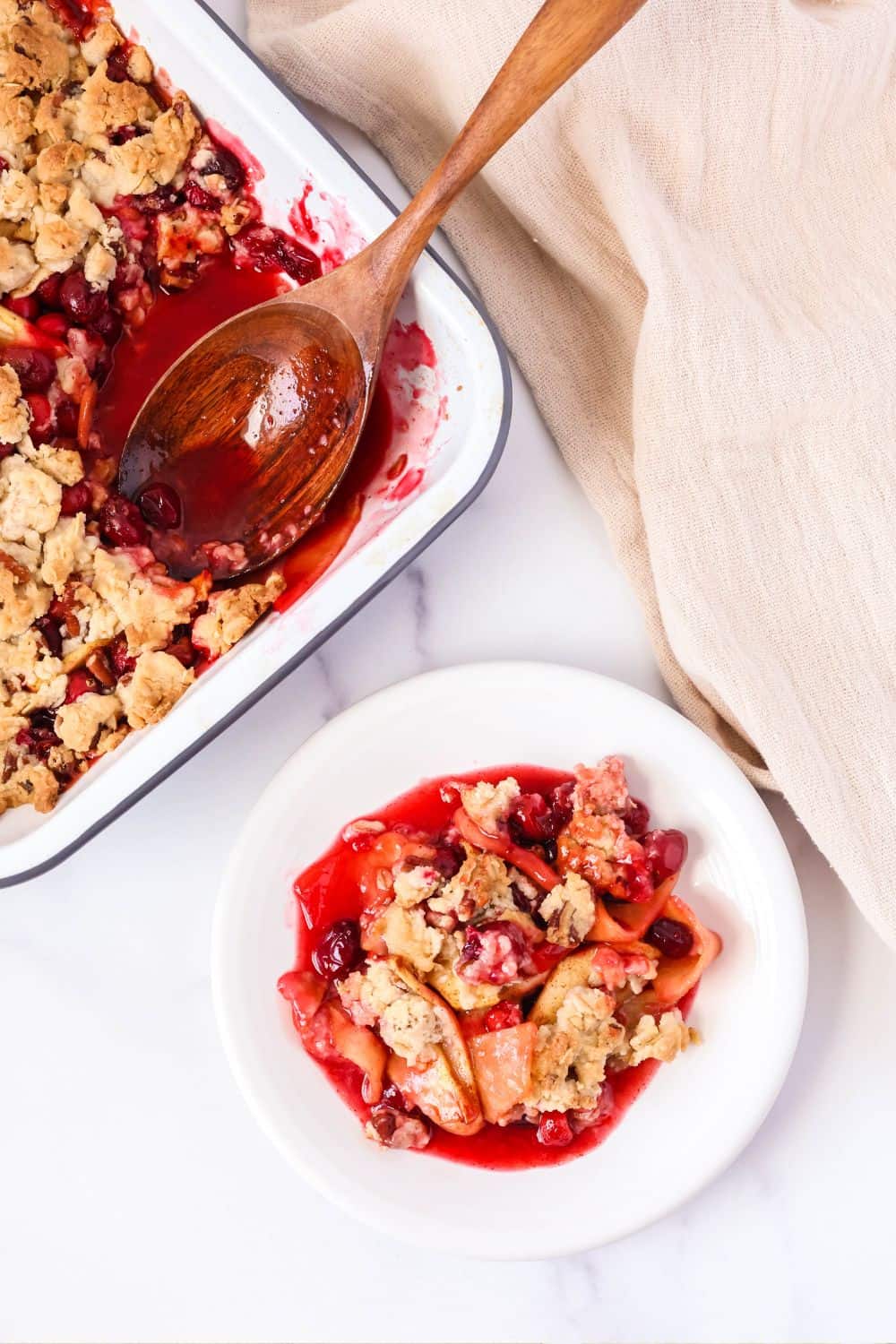 Overhead view of a white plate with a serving of cranberry apple cobbler made with Bisquick baking mix; the pan of fruit cobbler is next to the plate.