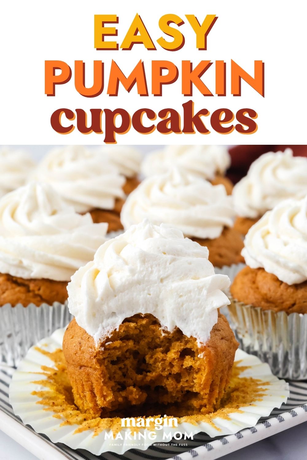 Close-up view of a pumpkin cupcake with a bite taken out of it, with several more pumpkin cupcakes in the background.