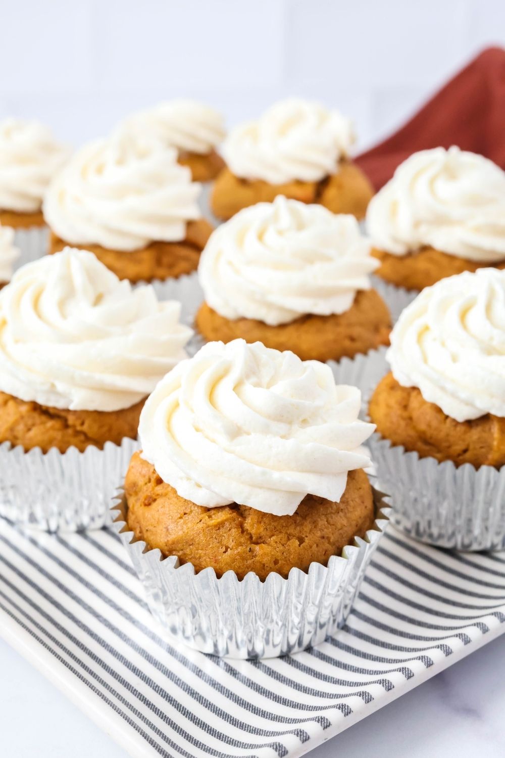 Fluffy pumpkin spice cupcakes topped with ermine frosting, served on a striped platter.