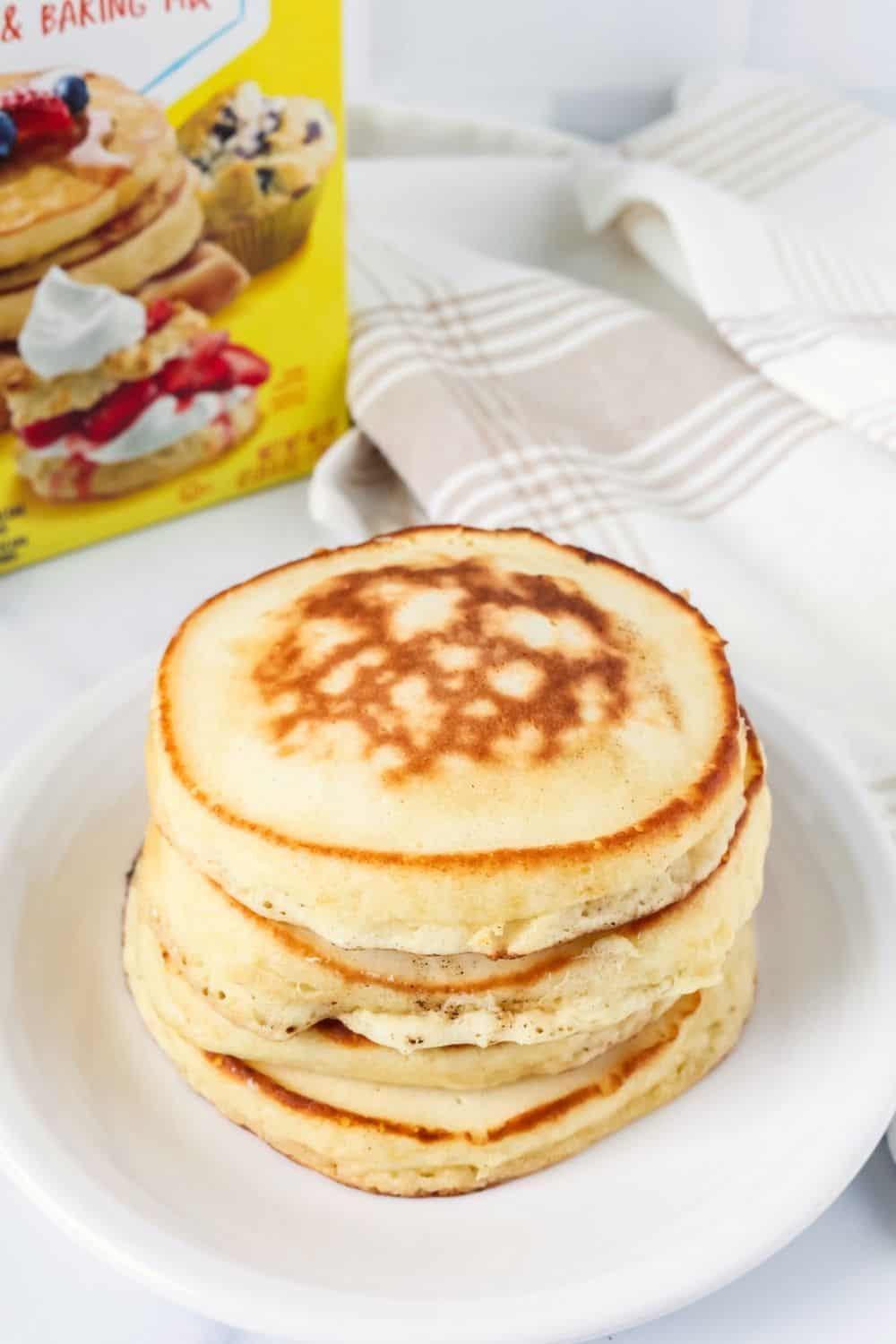 Four Bisquick pancakes served on a white plate, with a box of pancake mix in the background.