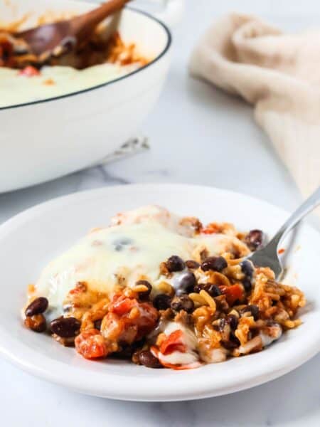 Cheesy Knorr taco rice casserole served on a white plate, with the pan of remaining casserole in the background.