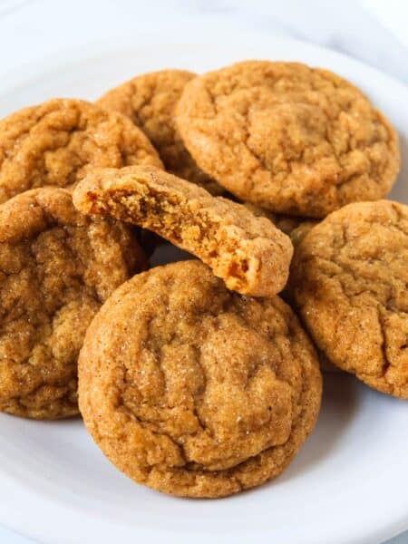 Several pumpkin molasses cookies on a white plate. One cookie has a bite taken out of it, showcasing the chewy interior.
