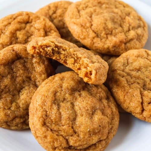 Several pumpkin molasses cookies on a white plate. One cookie has a bite taken out of it, showcasing the chewy interior.