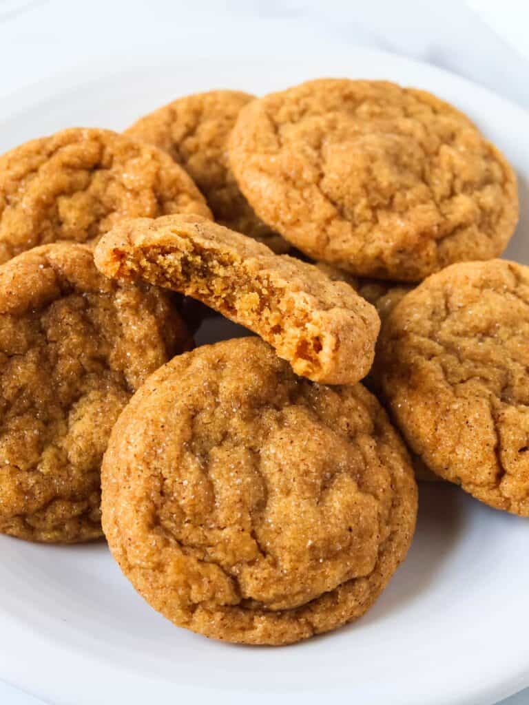 Several pumpkin molasses cookies on a white plate. One cookie has a bite taken out of it, showcasing the chewy interior.