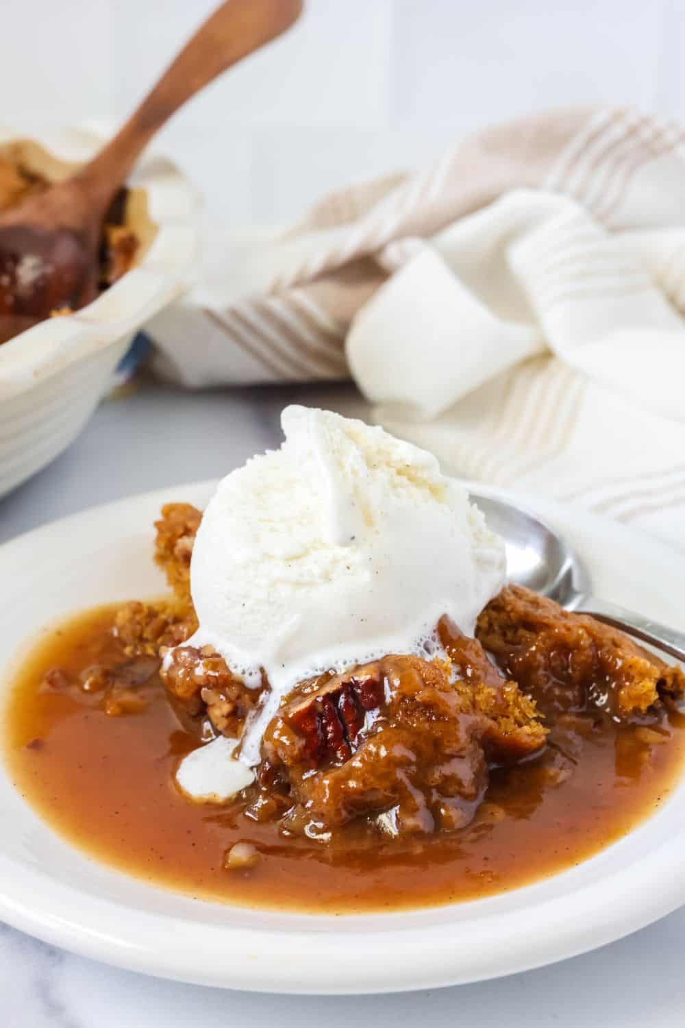 Close-up view of pumpkin pie cobbler on a white plate with a scoop of vanilla ice cream on top.