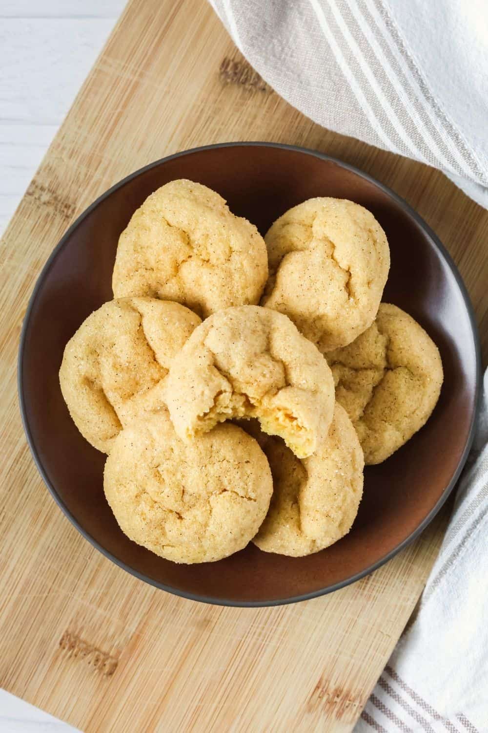 Overhead view of pumpkin spice sugar cookies on a brown plate atop a wooden cutting board.