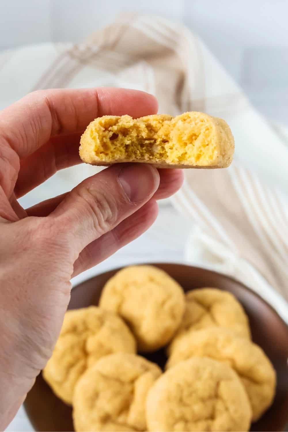 A woman's hand holds a soft and chewy pumpkin sugar cookie with a bite taken out of it.