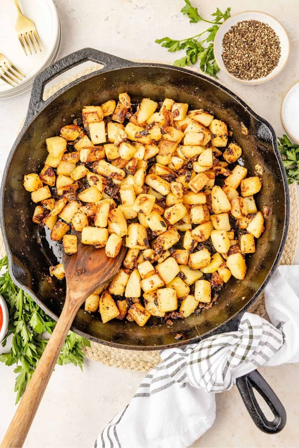 Southern fried potatoes in a cast iron skillet. A wooden spoon is in the skillet.
