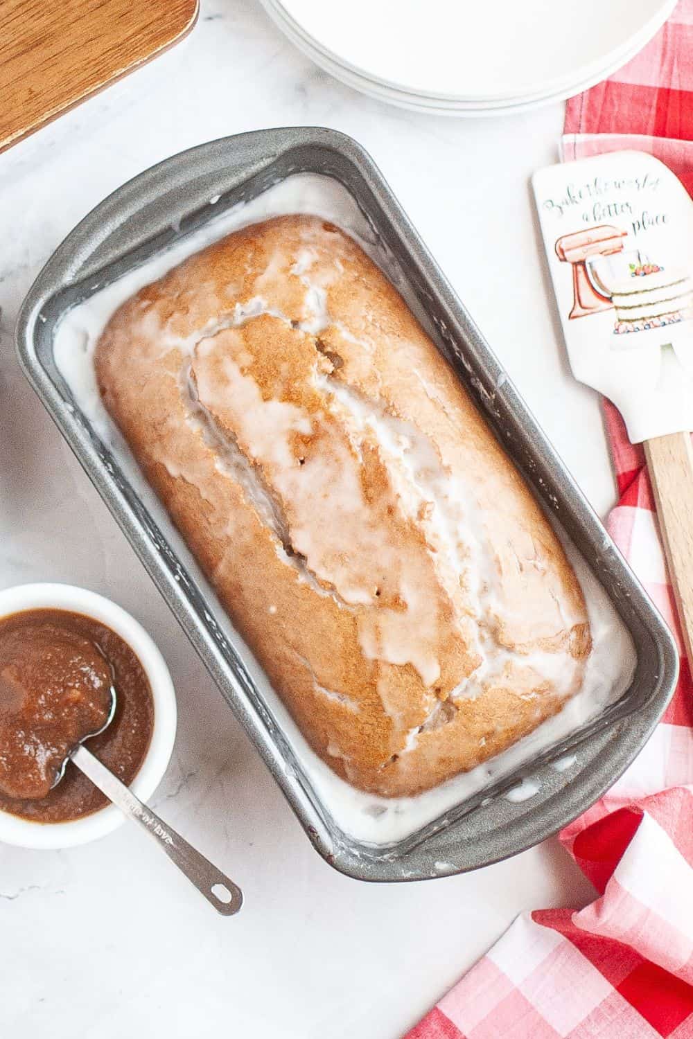 Overhead view of a loaf pan of freshly baked spiced apple butter bread that's been topped with a powdered sugar glaze.
