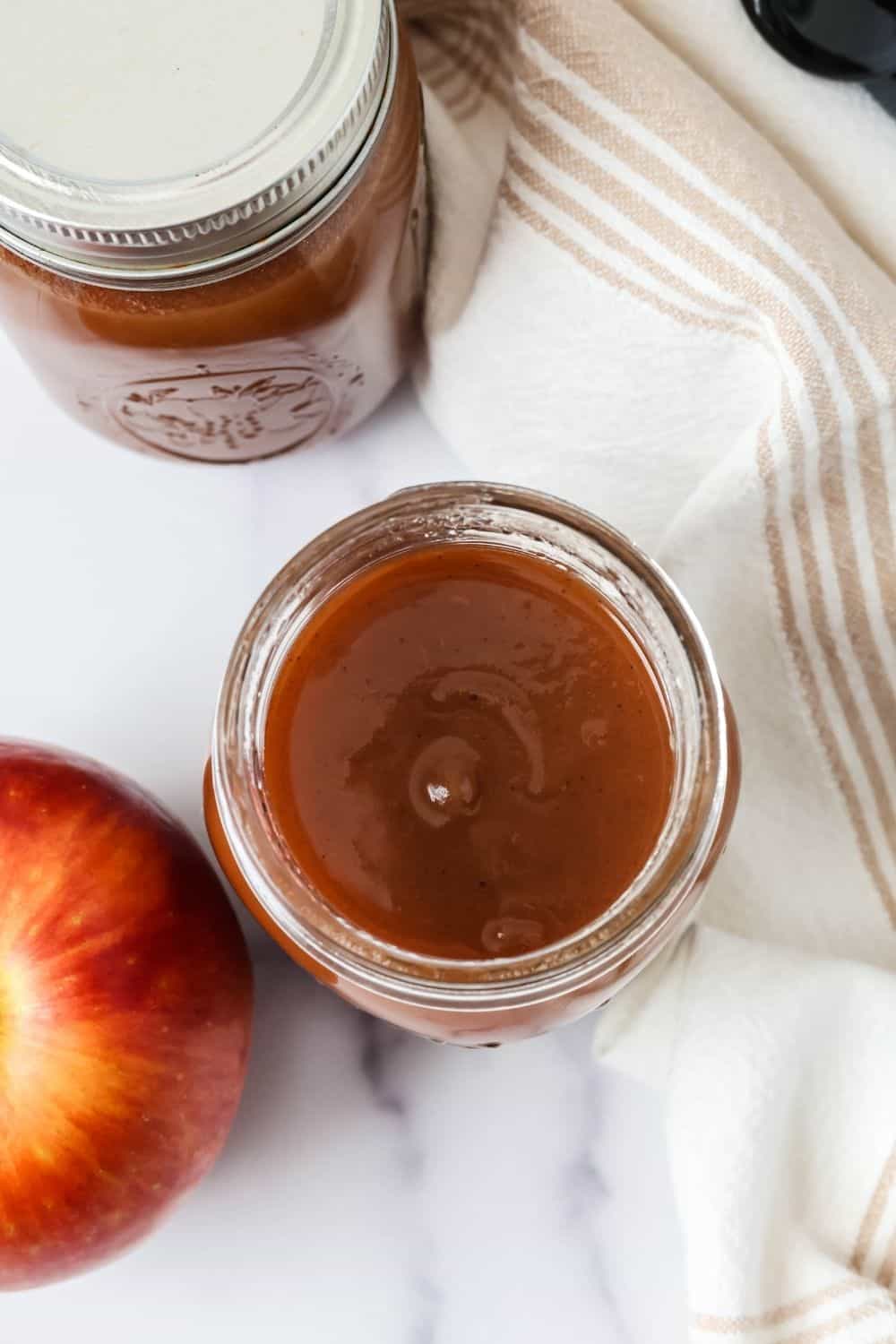 Overhead view of an open jar of spiced apple butter. A second closed jar is next to it, along with an apple.
