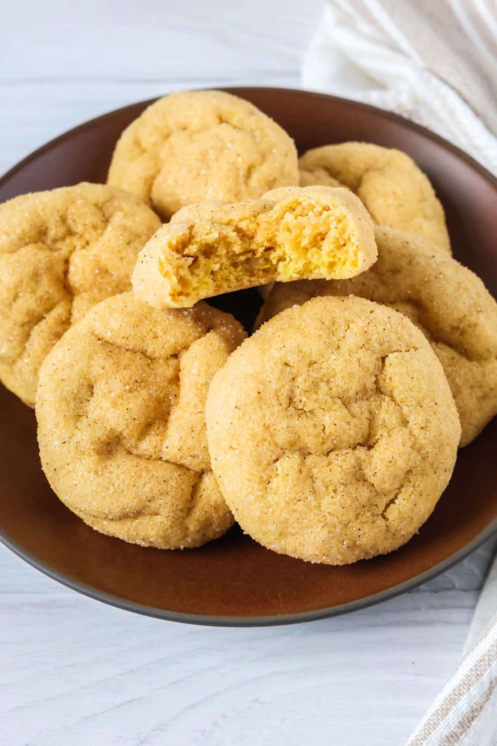 Several sugar cookies made with pumpkin puree are served on a brown plate. One has a bite taken out of it.