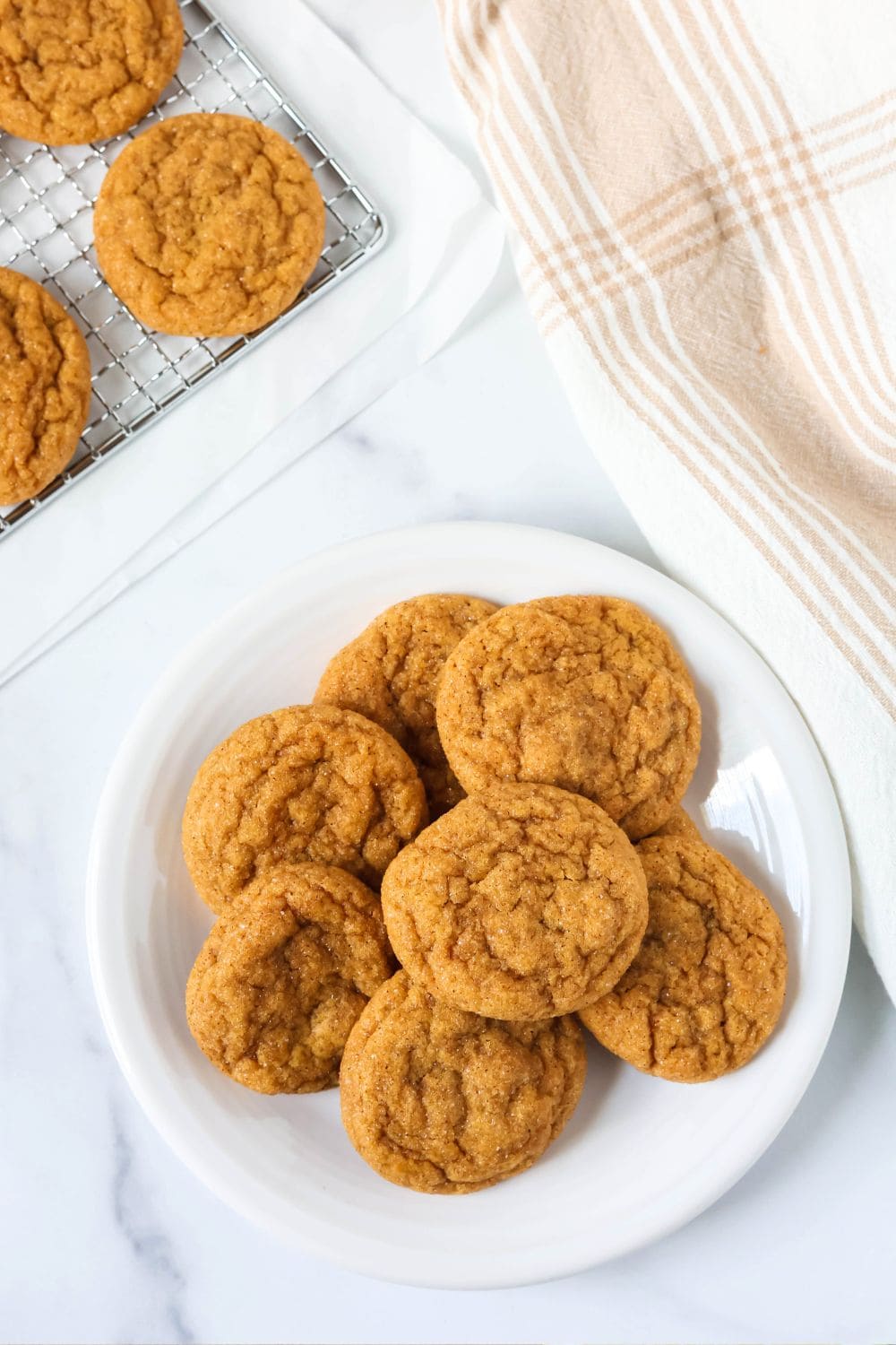 overhead view of several chewy molasses pumpkin cookies on a white plate, with more on a wire rack next to the plate.