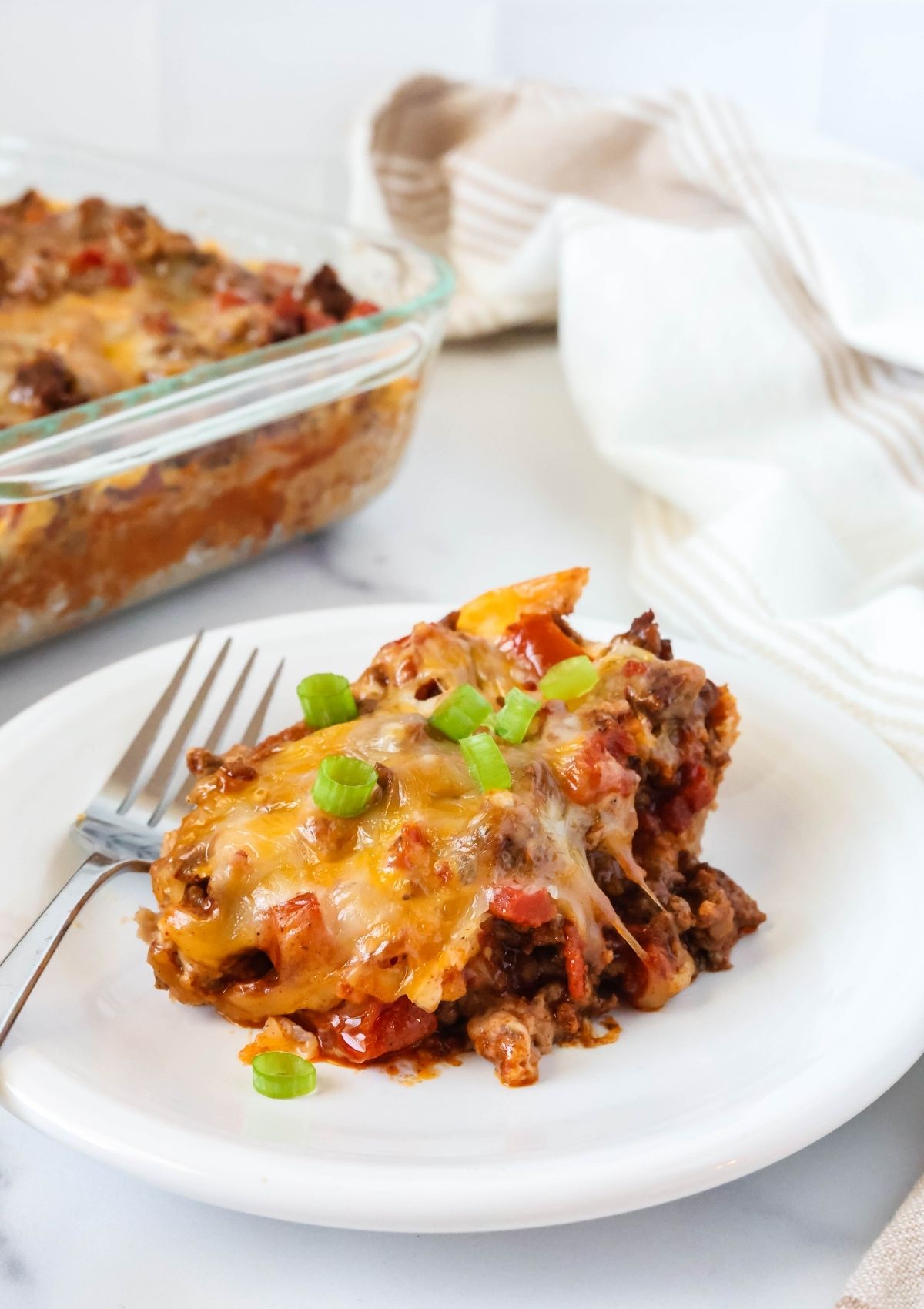 Bisquick burrito casserole served on a white plate, garnished with sliced green onions. The casserole dish is in the background.