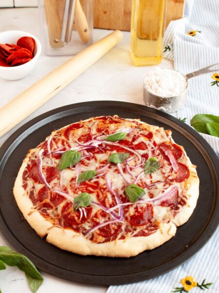 Bisquick pizza crust topped with sauce, cheese, pepperoni, red onions, and fresh basil. The pizza is still in the pan.