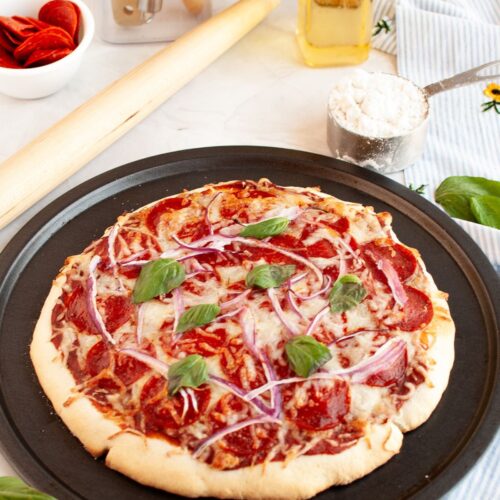 Bisquick pizza crust topped with sauce, cheese, pepperoni, red onions, and fresh basil. The pizza is still in the pan.