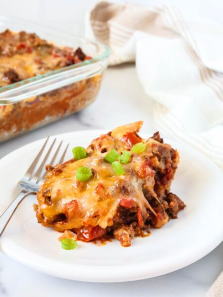 Bisquick taco casserole served on a white plate, garnished with green onions. The glass casserole dish is in the background.