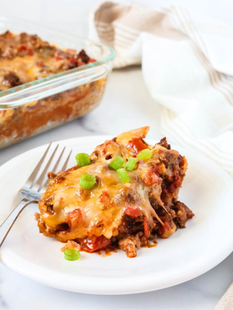 Bisquick taco casserole served on a white plate, garnished with green onions. The glass casserole dish is in the background.