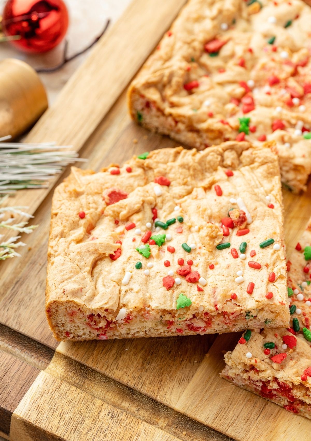 close-up view of a Christmas bar cookie topped with festive sprinkles on a wooden cutting board.