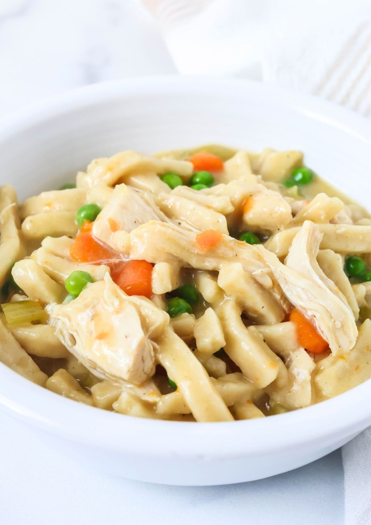 Chicken and noodles in a white bowl, showcasing the vegetables, tender noodles (made from frozen noodles), and chunks of chicken breast in a creamy sauce.