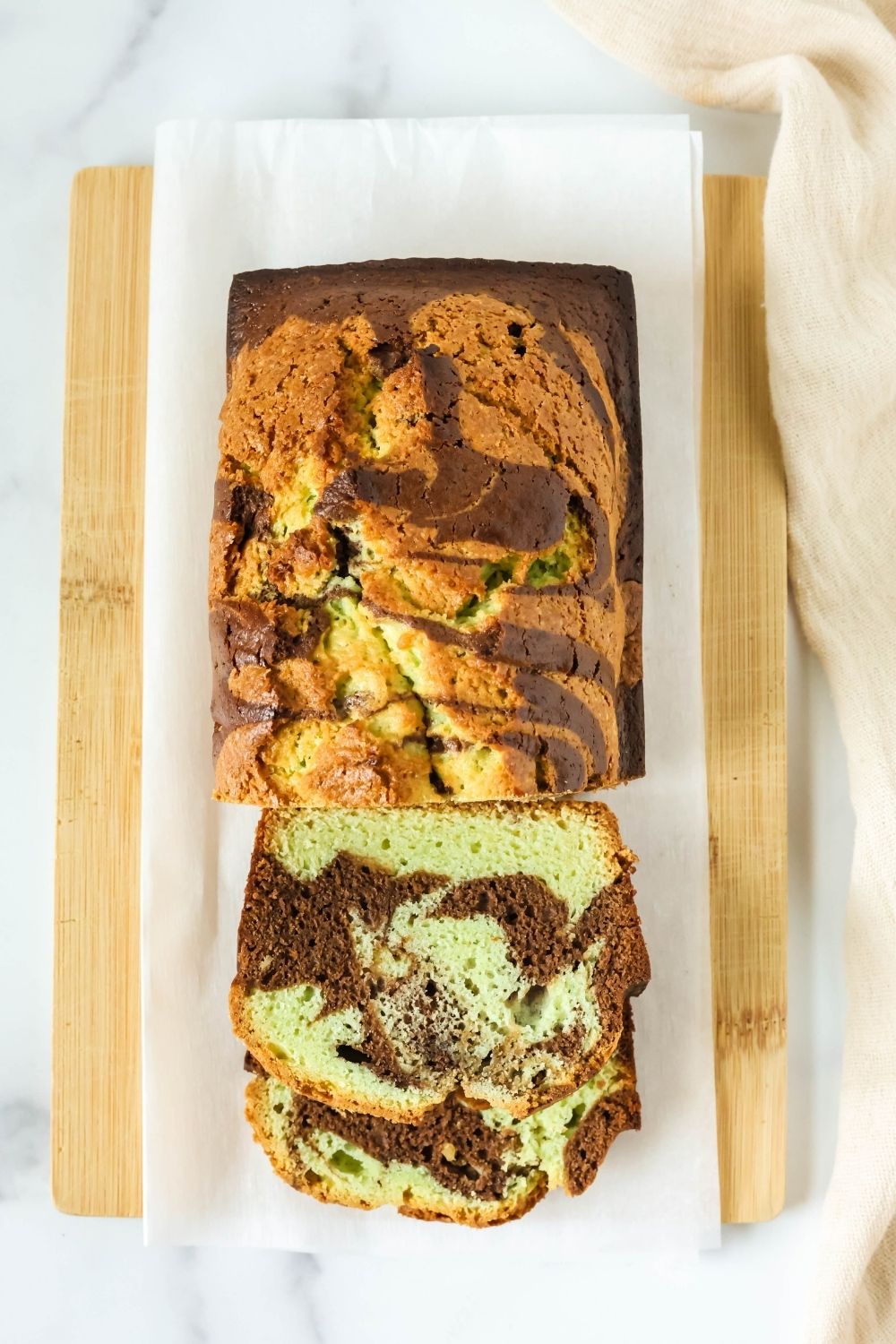 Overhead view of marbled chocolate pistachio loaf cake on a piece of parchment paper. A couple of slices have been cut from the loaf.