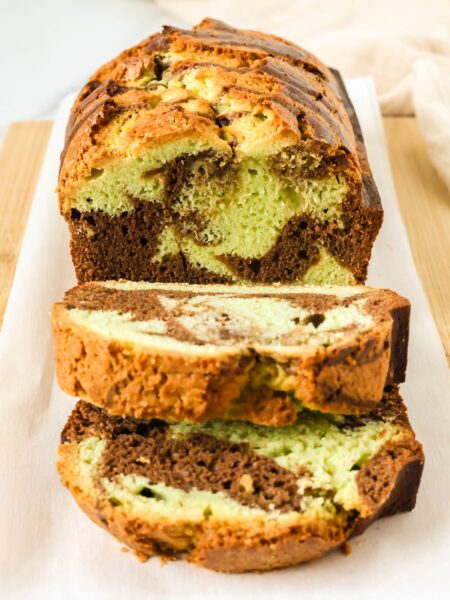 Chocolate pistachio loaf on a parchment-lined cutting board. A couple of slices have been cut from the loaf of quickbread, showing the marbled interior.