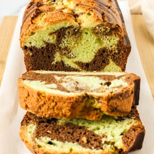 Chocolate pistachio loaf on a parchment-lined cutting board. A couple of slices have been cut from the loaf of quickbread, showing the marbled interior.