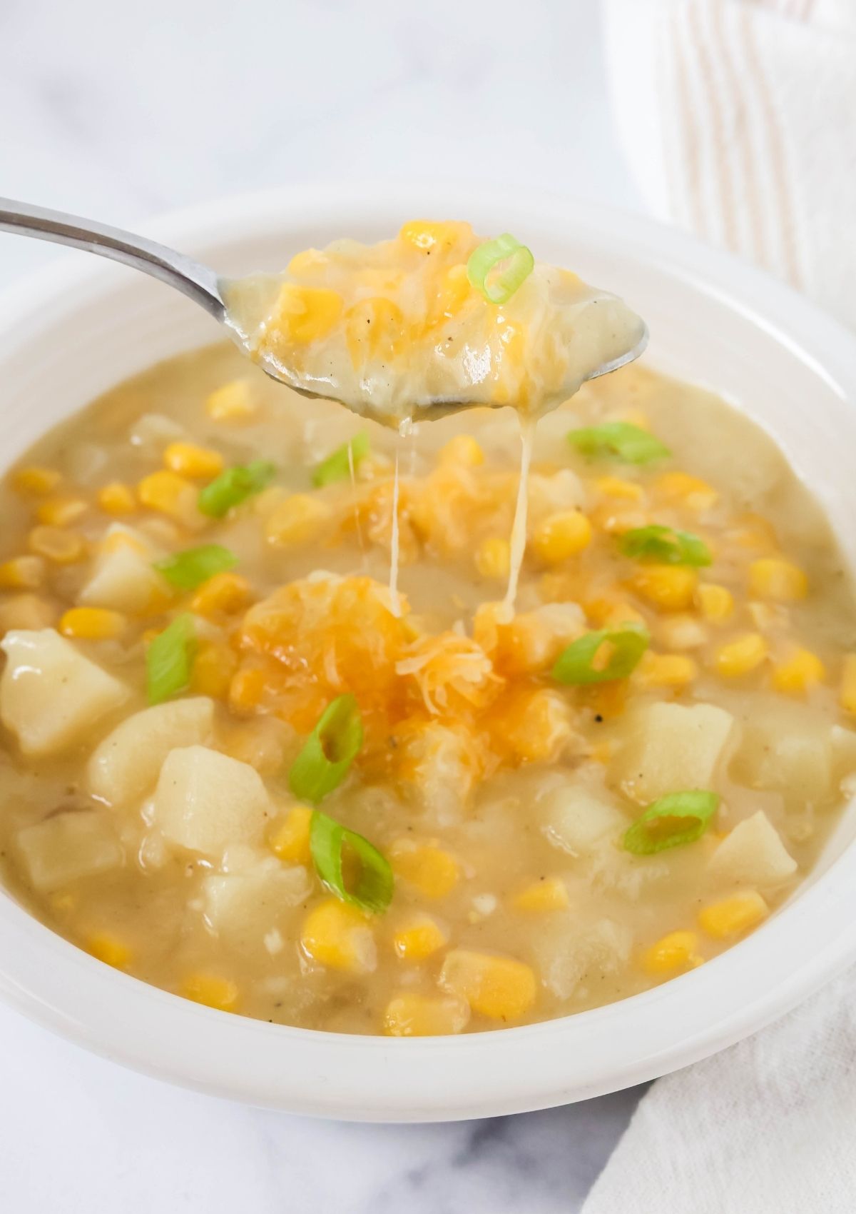 A spoon lifts a bite of corn and potato chowder from a white bowl.